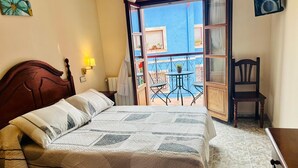 A hotel room with a bed, a bedside table, a lamp, a chair, and a balcony with a table and chairs. - Hotel Las Palmeras (Celorio)