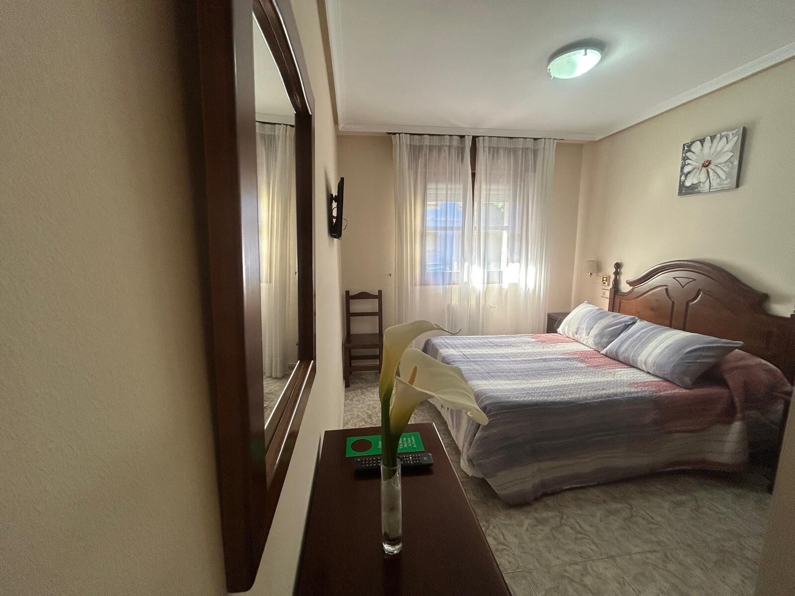 A bedroom with a bed, a chair, a desk with a lamp, and a mirror.