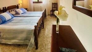 A hotel room with two beds, a desk with a remote control, a mirror, and a window with curtains. - Hotel Las Palmeras (Celorio)