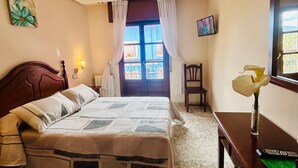 A bedroom with a bed, a desk, a chair, a TV, and a window with curtains. - Hotel Las Palmeras (Celorio)