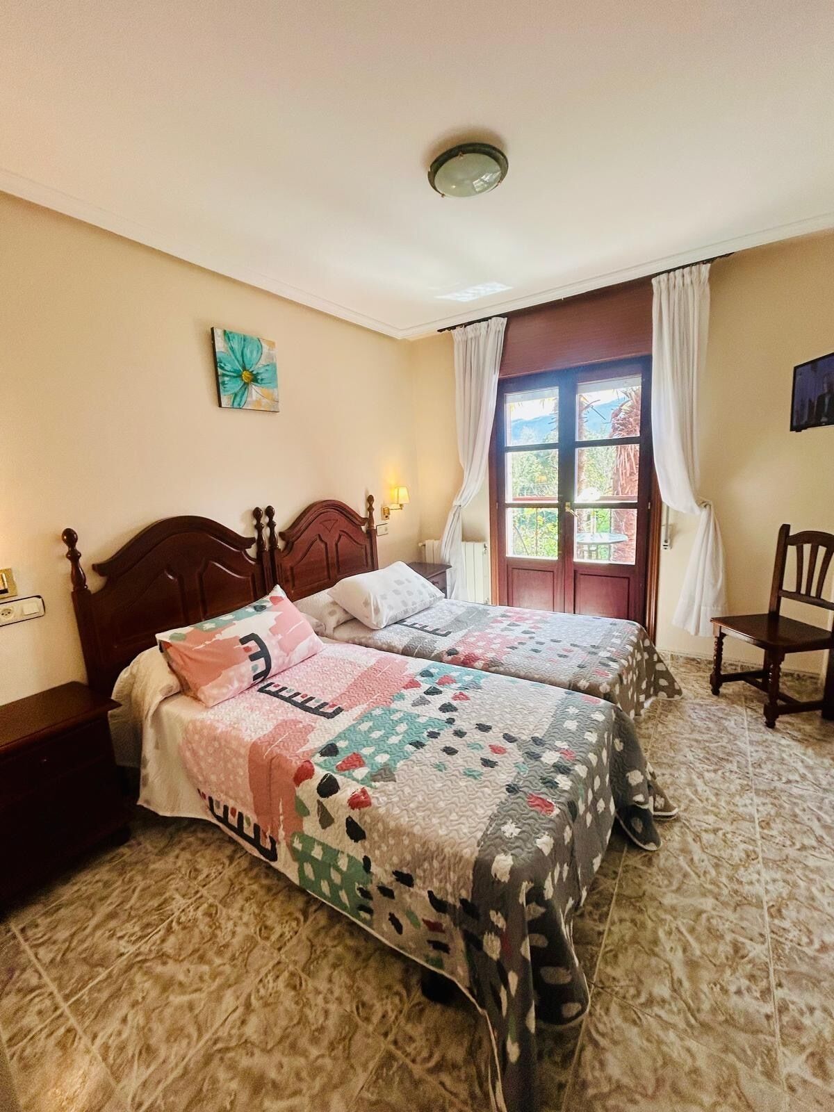 A room with two wooden beds, a small table, a chair, and a window with curtains.