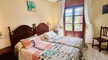 A room with two wooden beds, a small table, a chair, and a window with curtains.