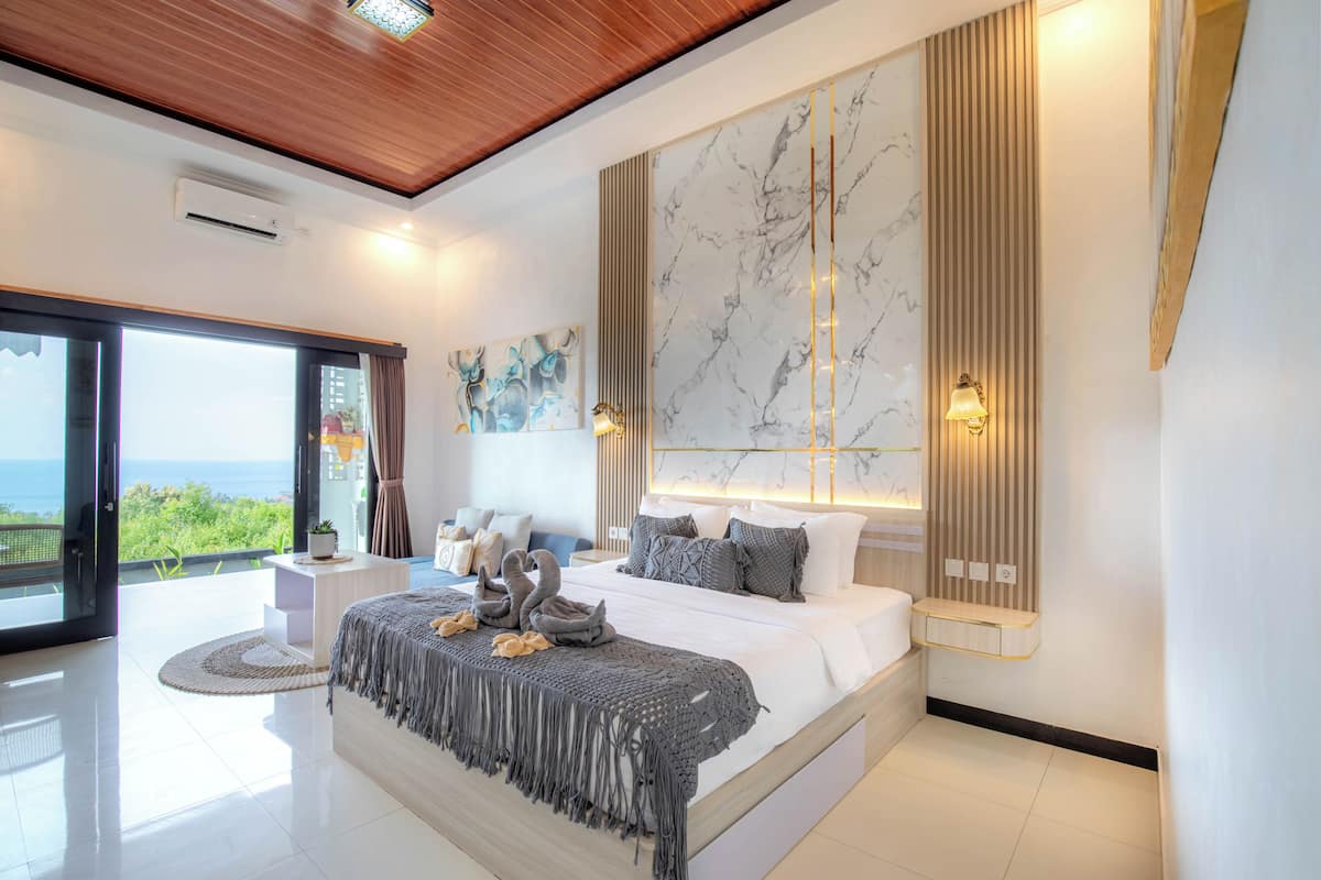 A modern bedroom with a large bed, a view of the outdoors, and a marble wall.