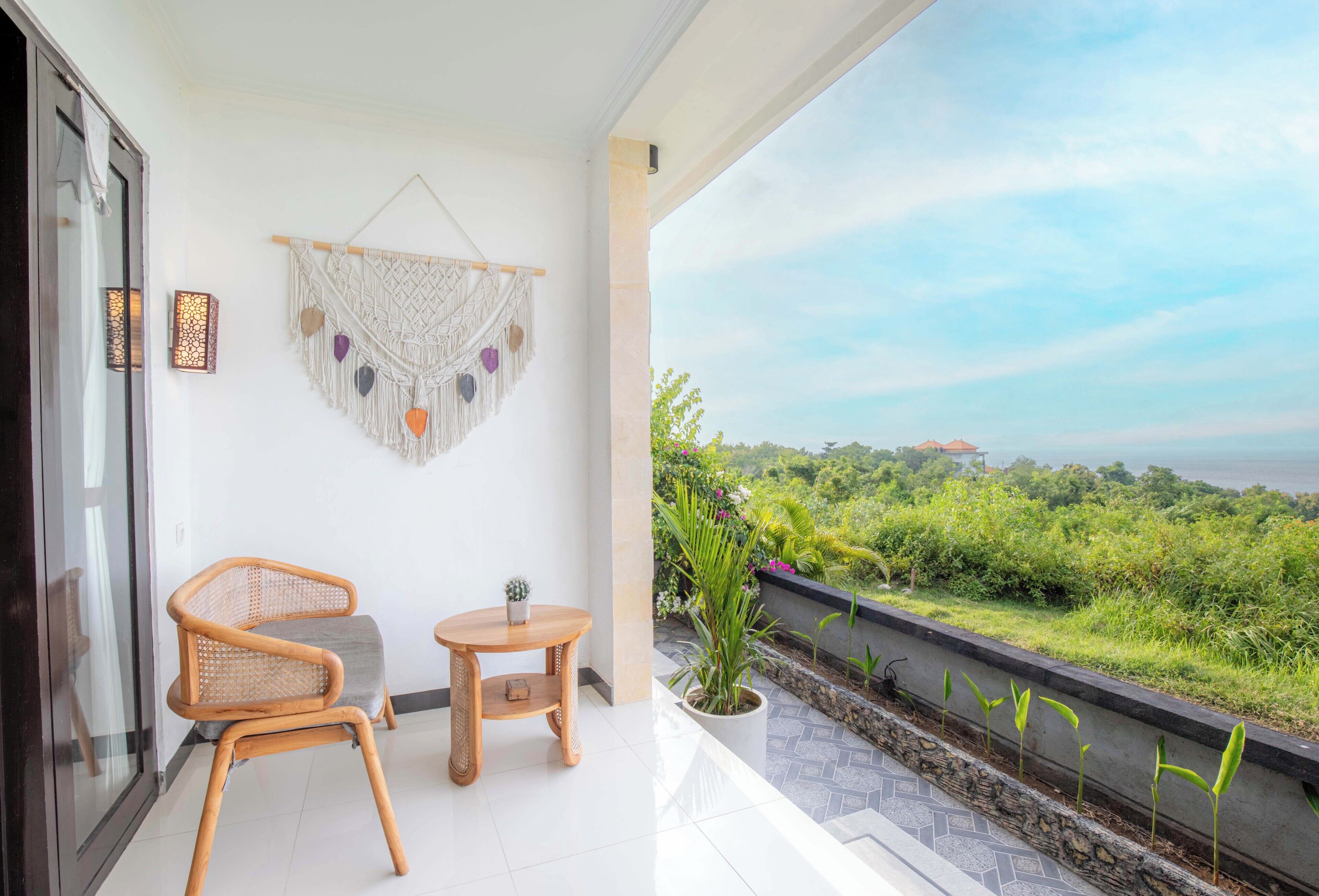 Een balkon met een rieten stoel, een klein rond tafeltje en een macramé wanddecoratie.