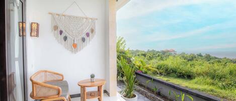A balcony with a wicker chair, a small round table, and a macrame wall hanging.