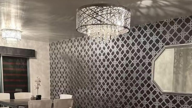 Un salon moderne avec un canapé en cuir noir, une table à manger avec des chaises, un lustre et un mur décoré de motifs.