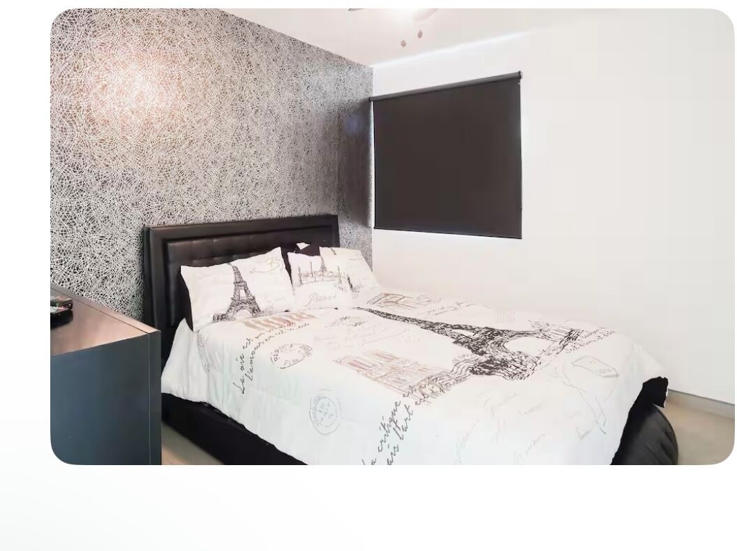 A bedroom with a bed, a nightstand, a window with blinds, and a textured wall.