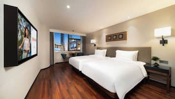 A hotel room with two beds, a desk, a chair, and a large window with a city view.