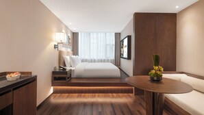 Moderni hotellihuone, jossa on sänky, yöpöytä, lamppu ja pieni pöytä, jonka päällä on maljakko.