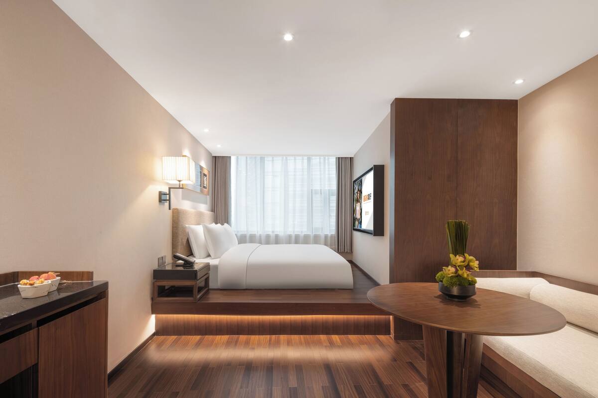 Et moderne hotelværelse med seng, sengebord, lampe og et lille bord med en vase.