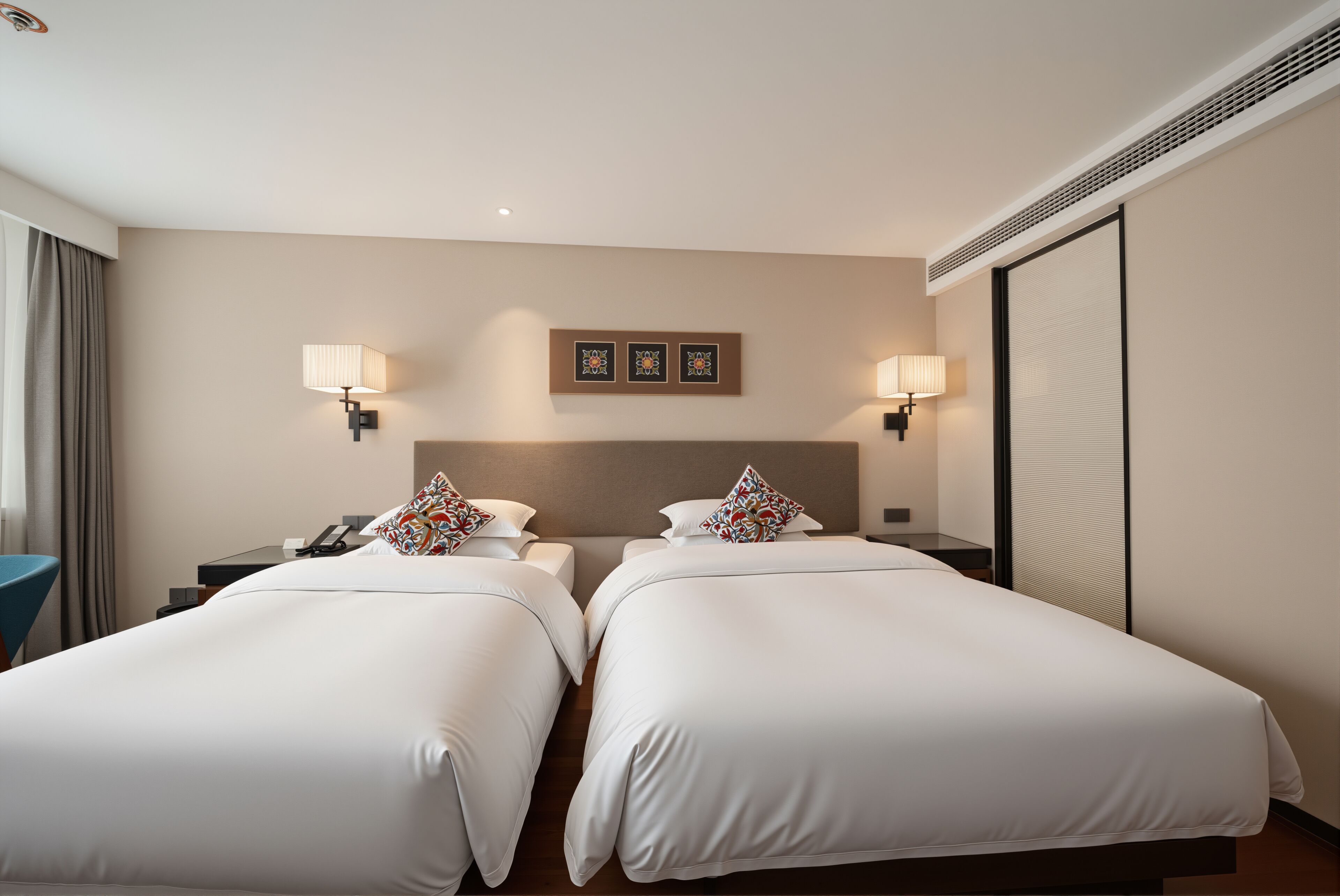 Habitació d'hotel amb dos llits, làmpades de nit, una tauleta de nit, un telèfon i un quadre penjat a la paret.