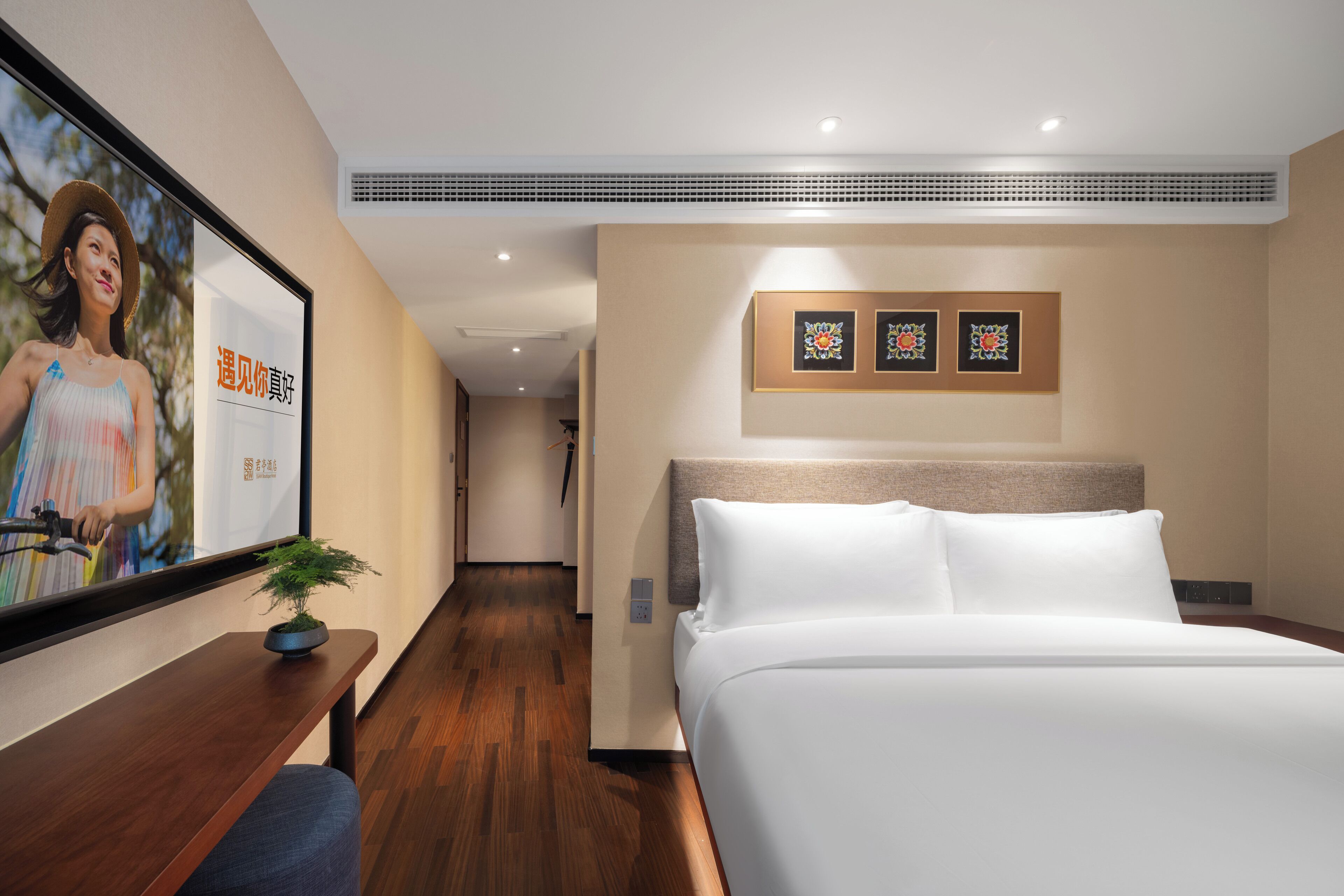Une chambre d’hôtel avec un grand lit, un bureau agrémenté d’une plante et des œuvres d’art encadrées accrochées au mur.