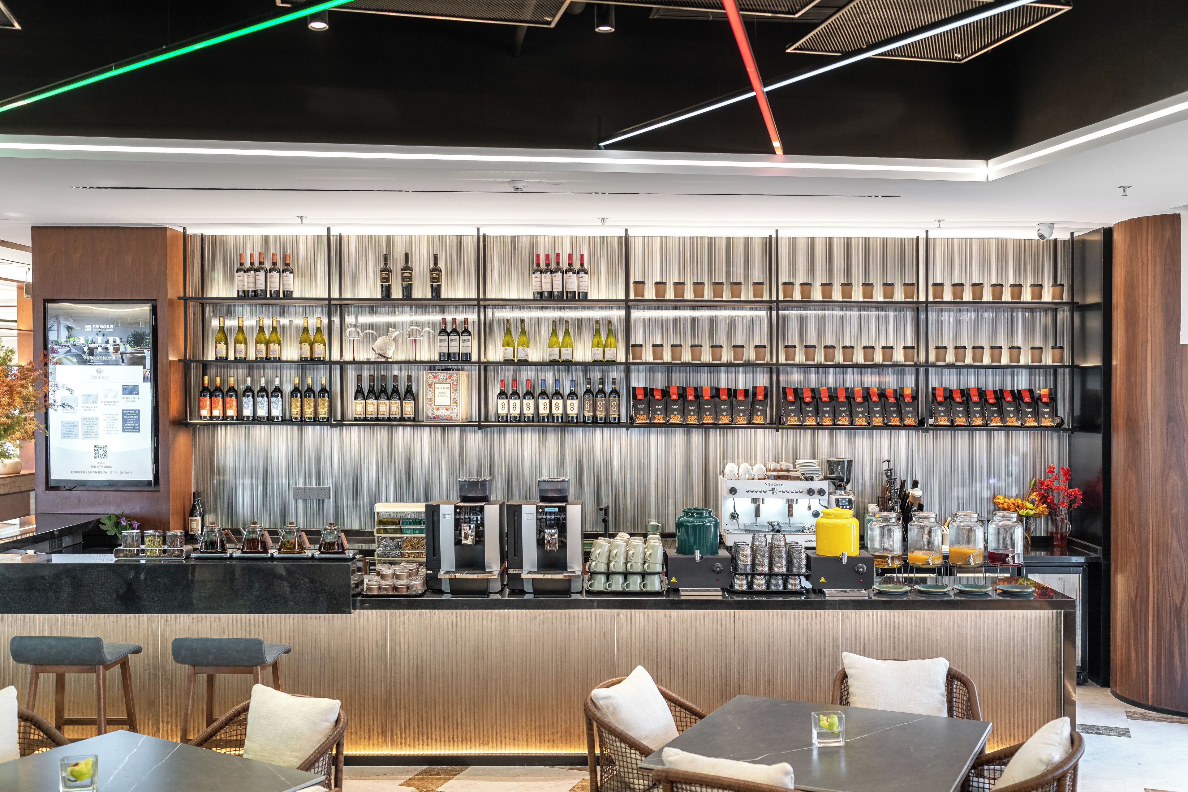 A modern bar area with a variety of wine bottles, coffee machines, and seating arrangements.