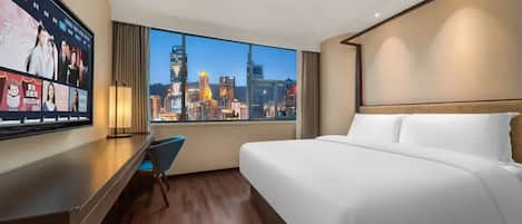 Habitación de hotel con cama, escritorio y un amplio ventanal con vista a la ciudad.
