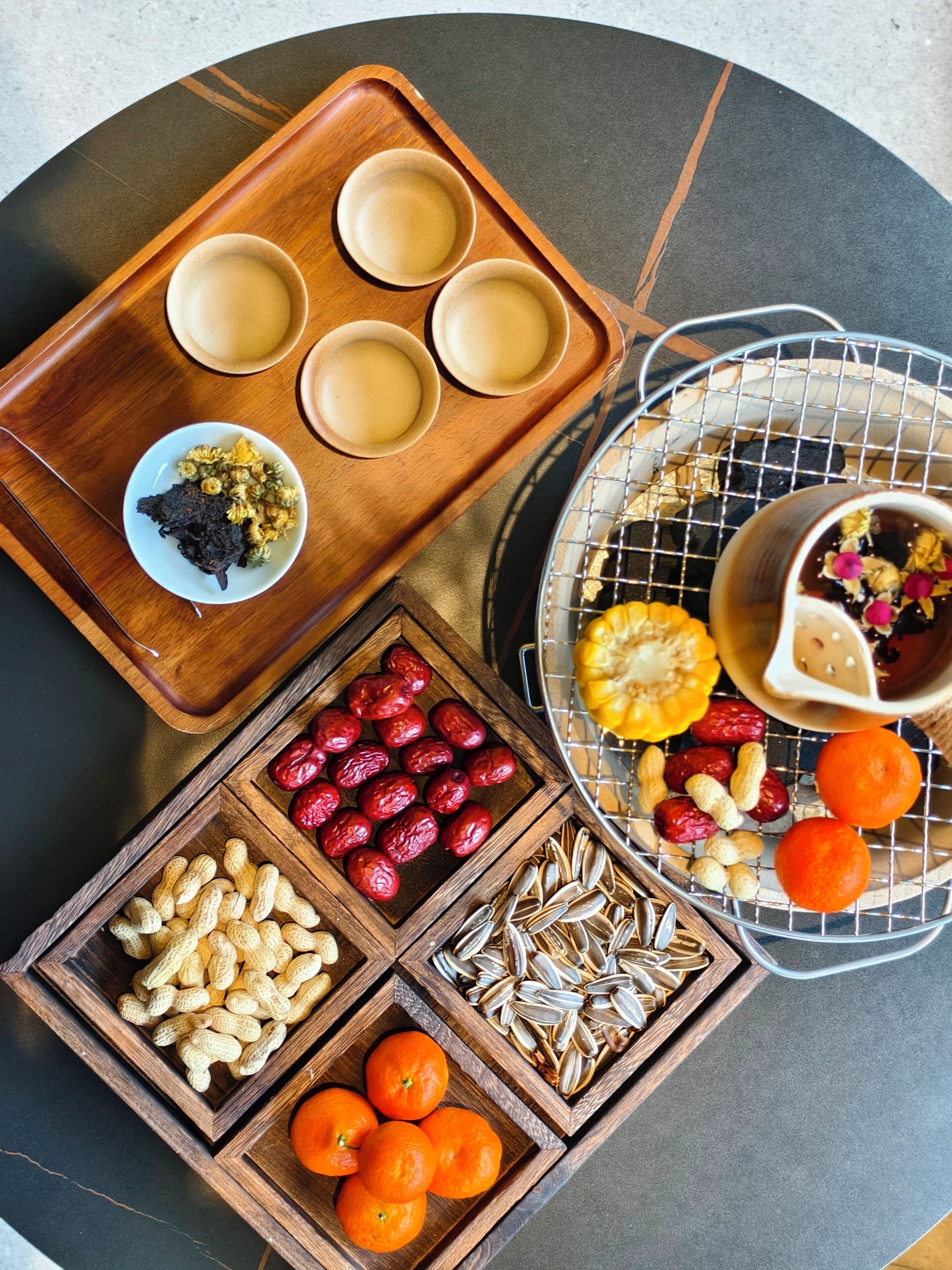 A wooden tray with bowls and a wire basket containing various snacks and fruits.
