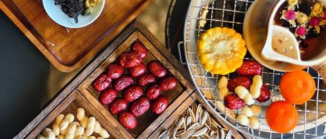 A wooden tray with bowls and a wire basket containing various snacks and fruits.