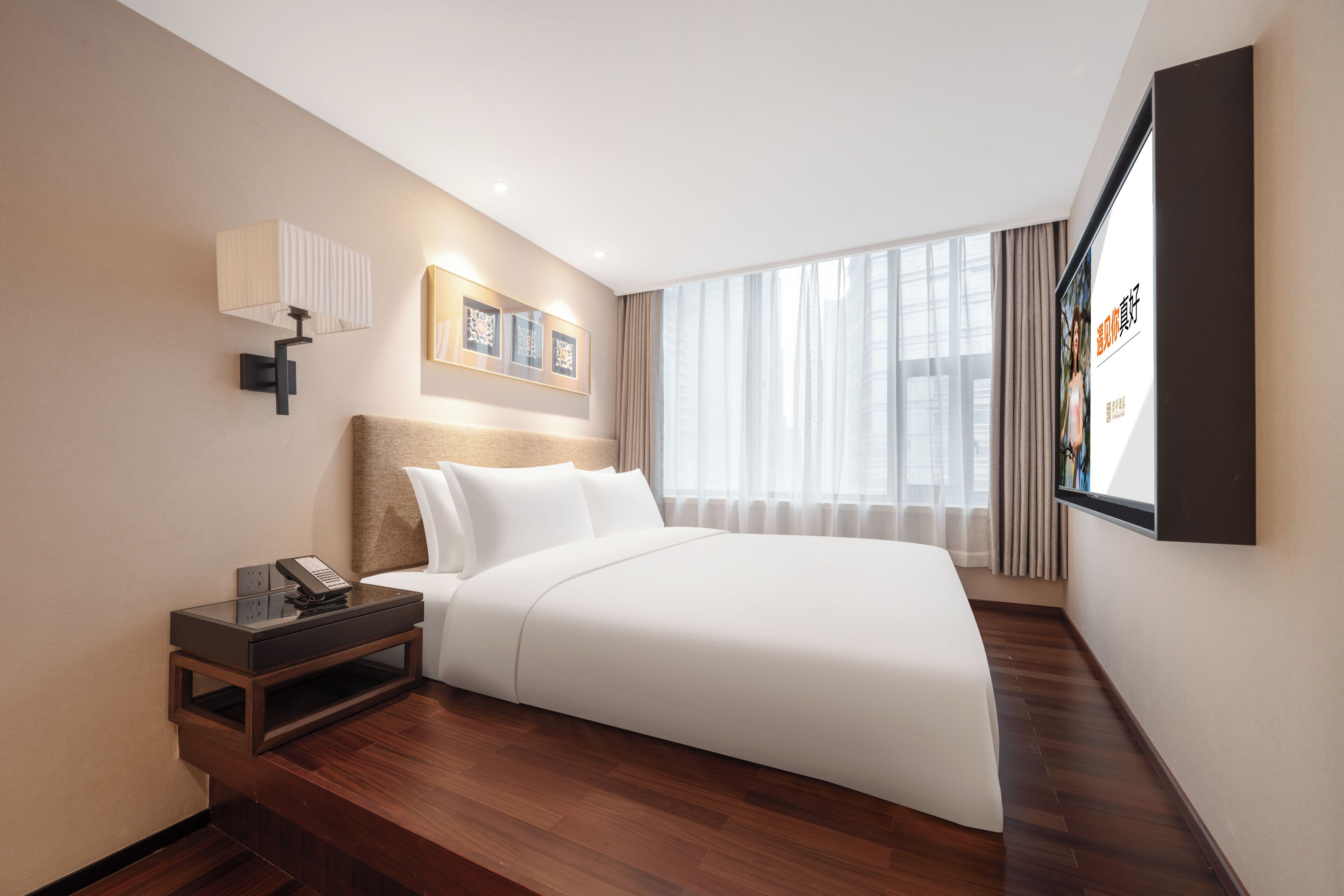 Een moderne hotelkamer met een net opgemaakt bed, een nachtkastje met een lamp en een groot raam met gordijnen.