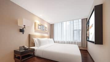 Una habitación de hotel moderna con una cama bien hecha, una mesita de noche con lámpara y un ventanal con cortinas.