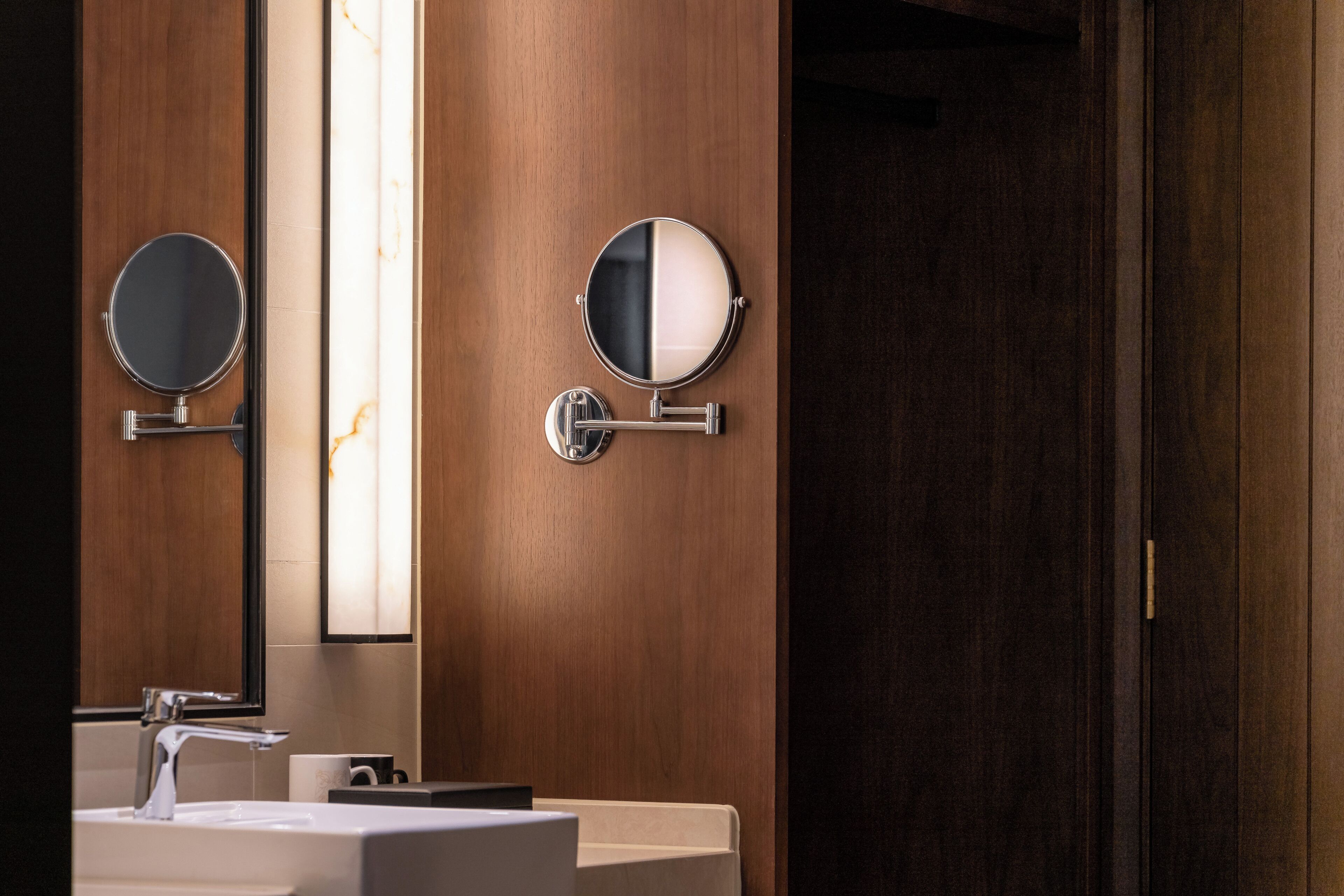Un baño moderno con tocador de madera, un espejo redondo y una lámpara de pared.