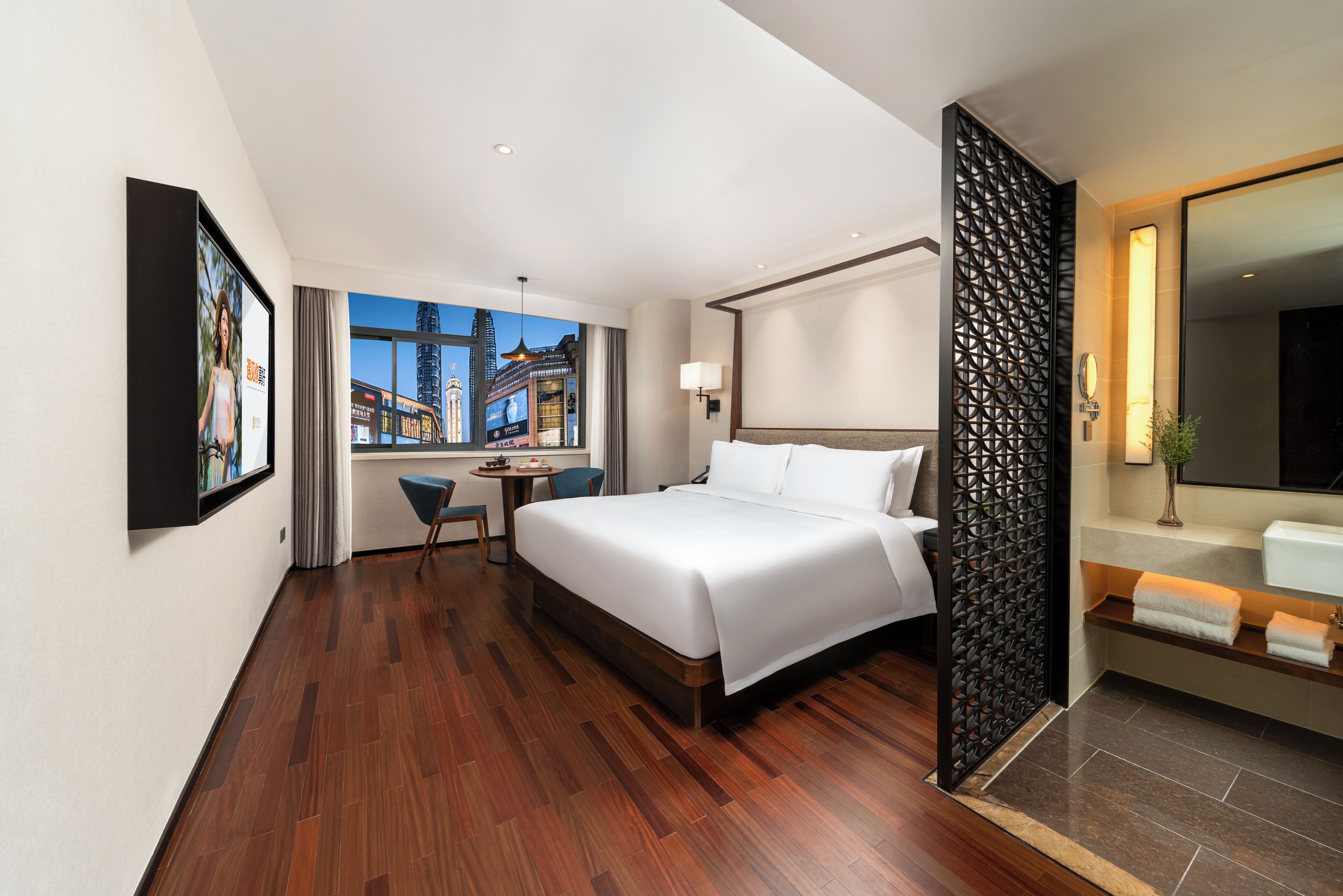 A modern hotel room with a large bed, a desk, and a view of a cityscape.
