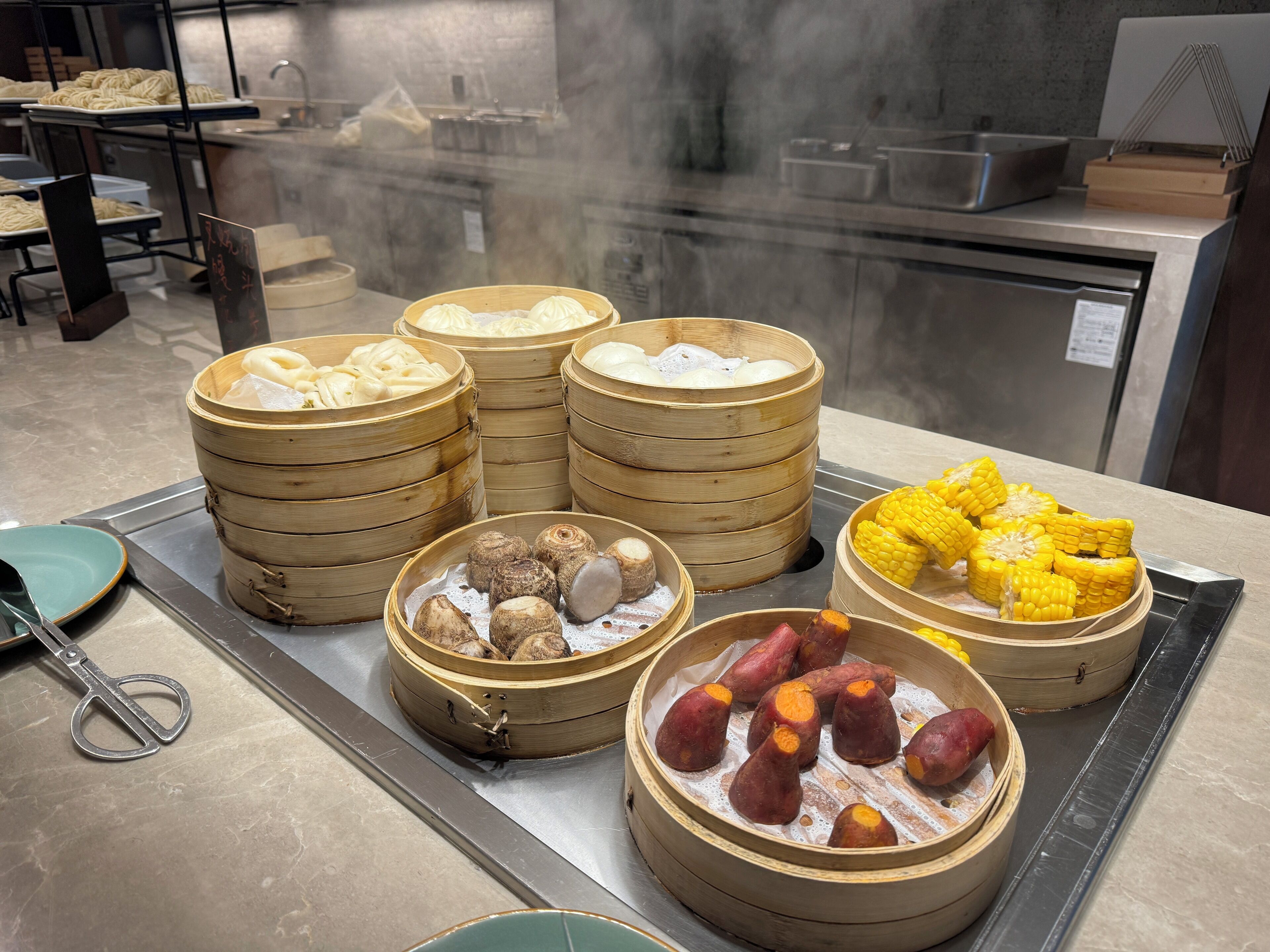 Une cuisine contenant divers aliments, notamment des cuiseurs à vapeur en bambou avec des raviolis et des patates douces, ainsi qu’une planche à découper avec un couteau.