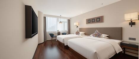 A hotel room with two beds, a TV, a desk, and a window.