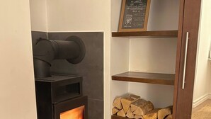Un poêle à bois moderne avec des flammes apparentes, une étagère à bois et un tableau noir servant de menu, placé au-dessus.