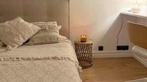 Une chambre à coucher avec un lit, une table de chevet avec une lampe, une petite table d’appoint avec une bougie et deux tableaux encadrés accrochés au mur.