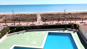 A pool area with two rectangular pools, a pathway leading to the beach, and a view of the ocean.