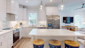 A modern kitchen with white cabinetry, stainless steel appliances, a large island with stools, and pendant lighting.