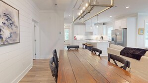 A modern kitchen with white cabinetry, a wooden dining table, and a black sofa.