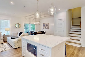 A spacious kitchen with a large island, pendant lights, and a view of the dining area. - Stylish New Luxury Home, Dog Friendly, Great Outdoor Spaces, BHI Club + Golf (Bald Head Island)