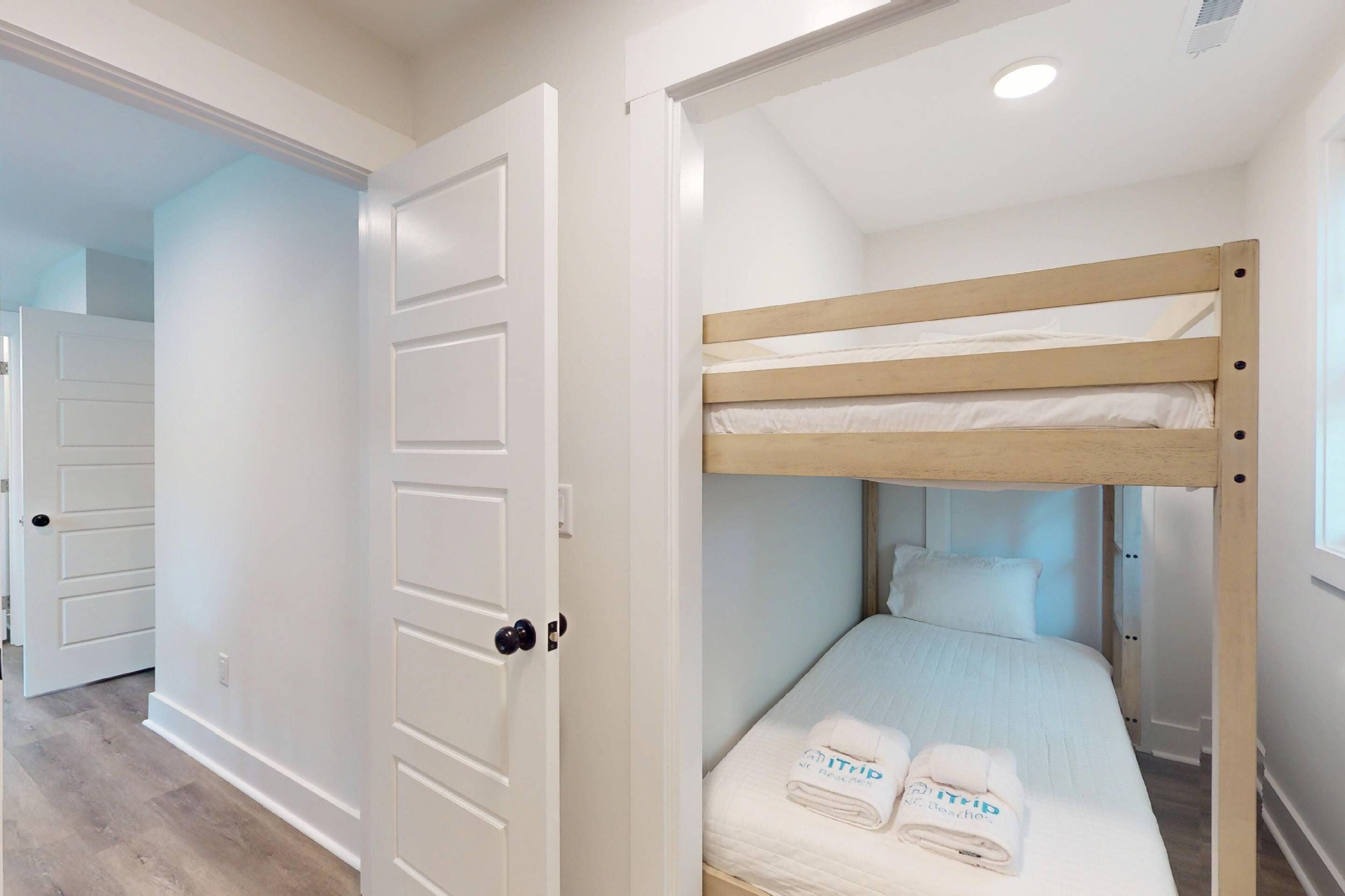Una cama litera con cabecera blanca, una puerta con picaporte negro y una toalla sobre la cama.