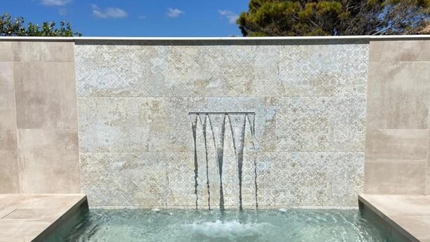 Una piscina con una cascada, rodeada por un muro de piedra.