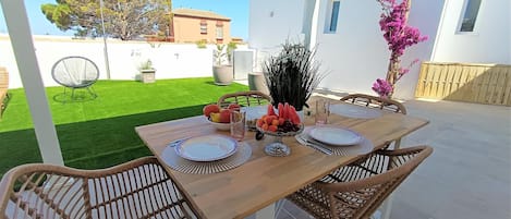 A patio with a wooden table set for four, surrounded by wicker chairs, with a white pergola overhead.