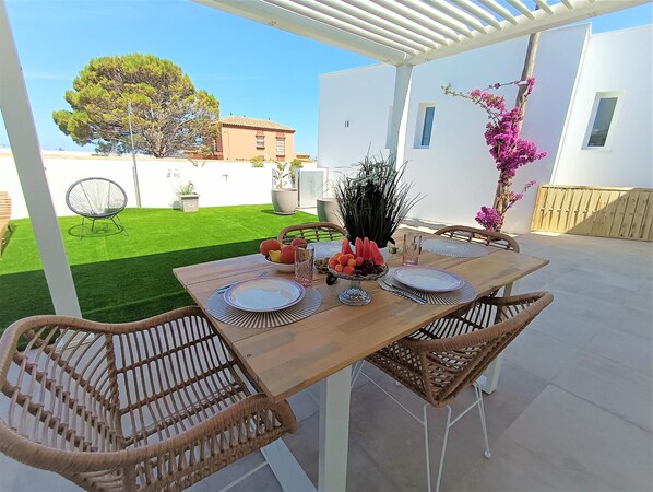 A patio with a wooden table set for four, surrounded by wicker chairs, with a white pergola overhead. - Suite La Buganvilla in Conil de la Frontera (Conil de la Frontera)