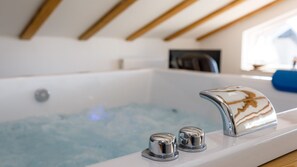 A modern bathroom with a bathtub, chrome fixtures, and wooden ceiling beams.