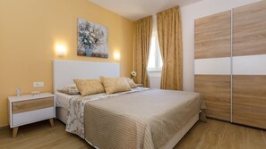 A bedroom with a bed, nightstand, bedside table, and a painting on the wall.