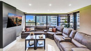 A modern living room with a sectional sofa, a coffee table, and a large window offering a city view. - Beachside Condo with Resort Amenities, Including Pools, Gym, and Bathtub 503 (Miami Beach)