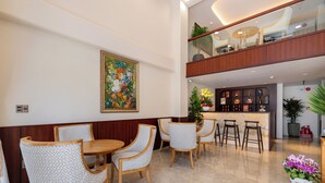A dining area with a wooden table and patterned chairs, a bar area with stools, and a large painting on the wall.