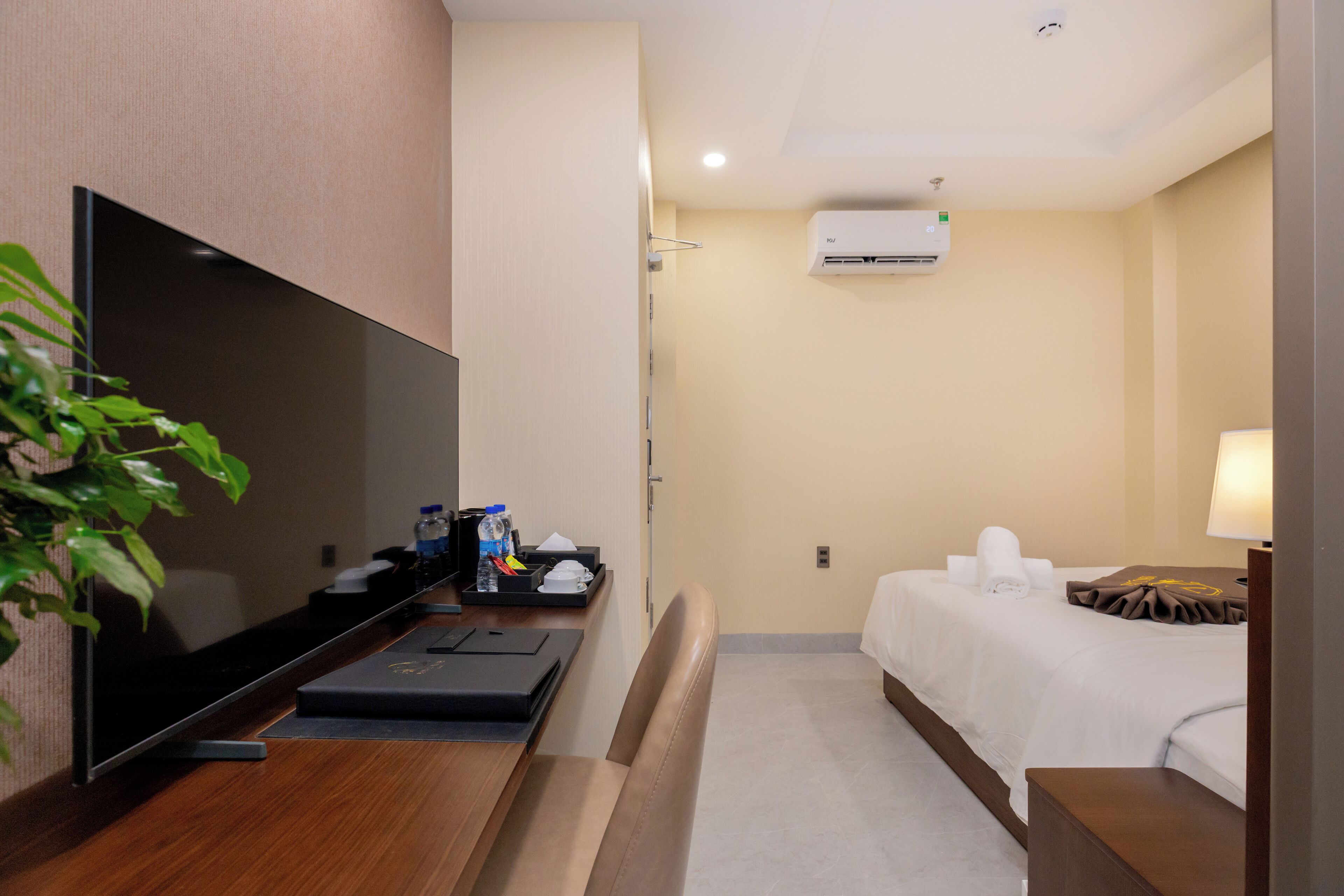Une chambre d’hôtel équipée d’une télévision à écran plat, d’un bureau avec un ordinateur portable, d’un lit avec du linge de lit blanc et d’une table de chevet avec une lampe.