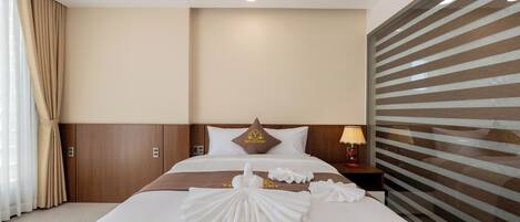 A hotel room with a neatly made bed, a headboard with a logo, a nightstand with a lamp, and a large window with blinds.
