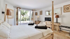 Un dormitorio amplio con cama con dosel, televisor, escritorio y un gran ventanal con vistas a zonas verdes.