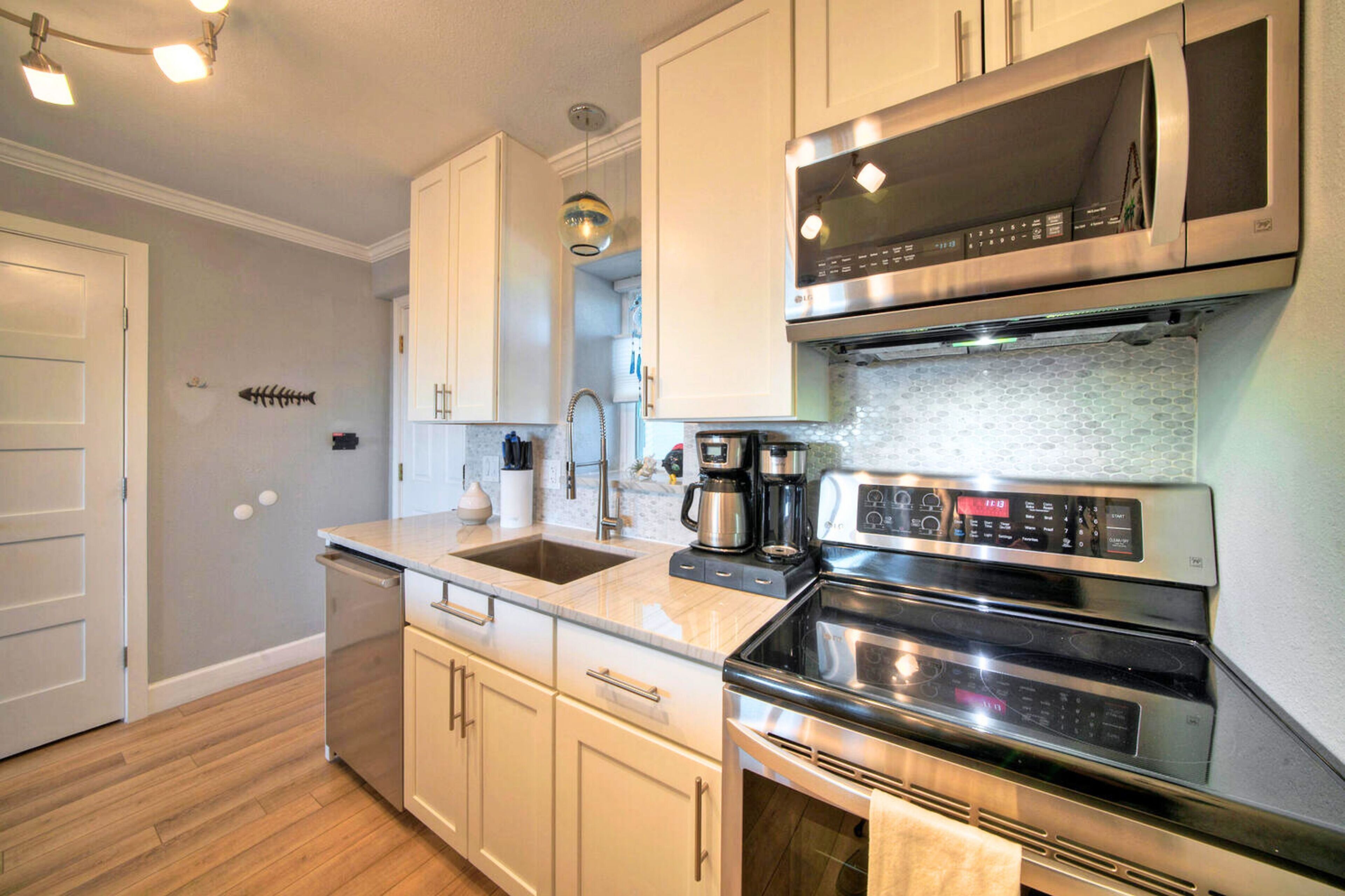 A modern kitchen with white cabinets, stainless steel appliances, and a wooden floor.