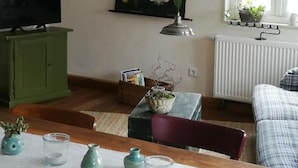 A living room with a television, a green cabinet, a table with decorative items, a hanging plant, and a window with a view of the outside. - Vacation apartment Am Schloßberg (Solingen)