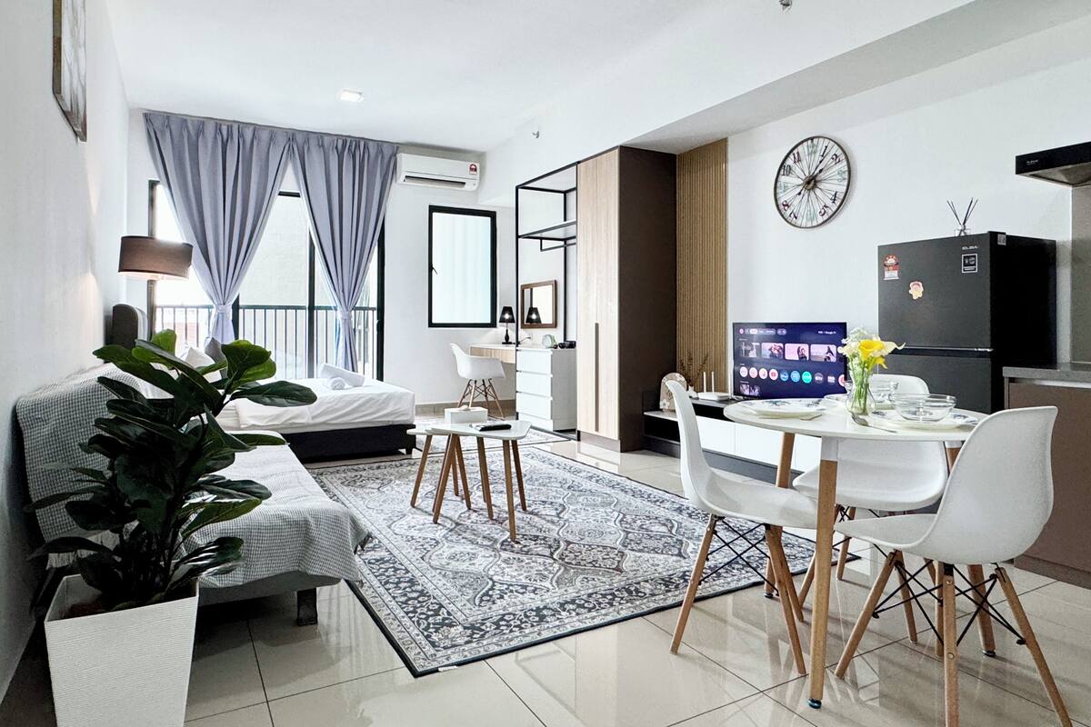 A modern hotel room with a bed, a desk, a dining area, and a kitchen.