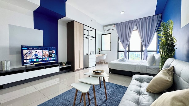 A modern living room with a flat-screen TV, a sofa, a coffee table, and a dining area. - Alinea Suites (Shah Alam)