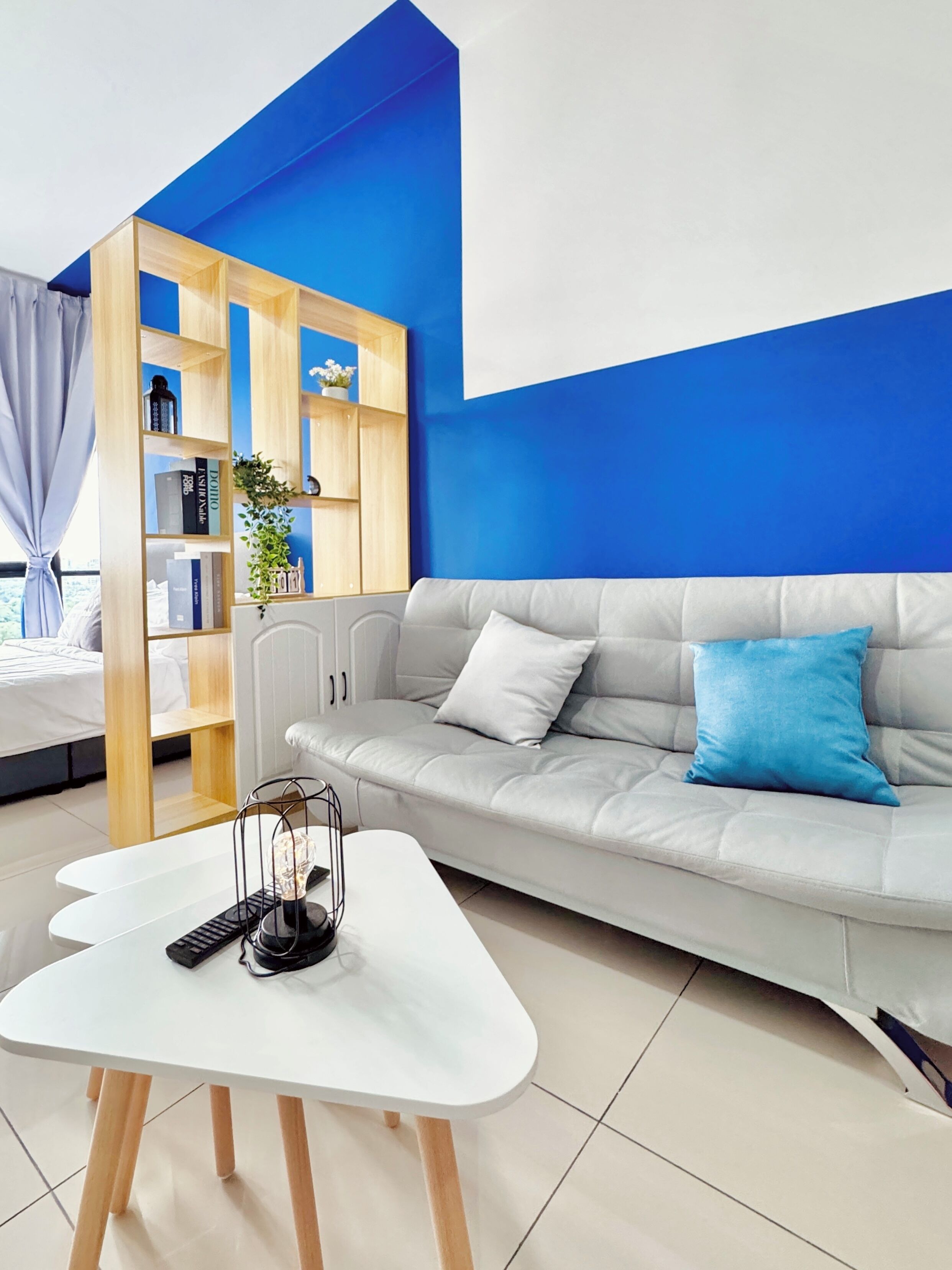 A modern living room with a grey sofa, a white coffee table, and a wooden bookshelf against a blue wall.