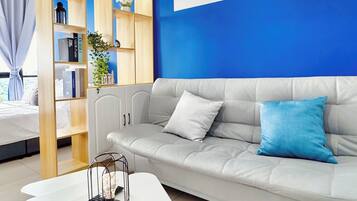 A modern living room with a grey sofa, a white coffee table, and a wooden bookshelf against a blue wall.