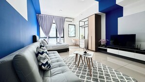 A modern living room with a sofa, a TV, and a dining area. - Alinea Suites (Shah Alam)